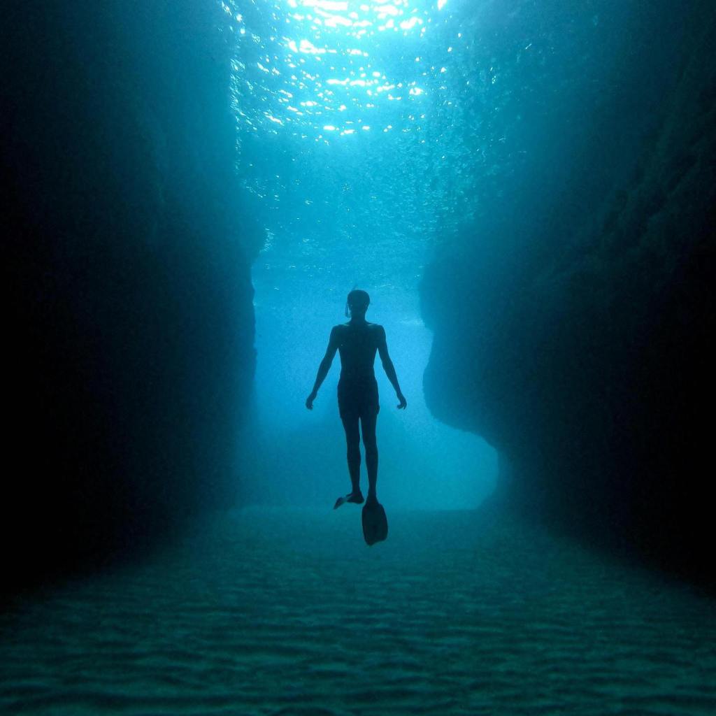 Silhouette of a freediver ascending through an underwater canyon, symbolizing bold exploration of marketing and SEO, and the pursuit of deeper insight through questioning assumptions and accepted norms.